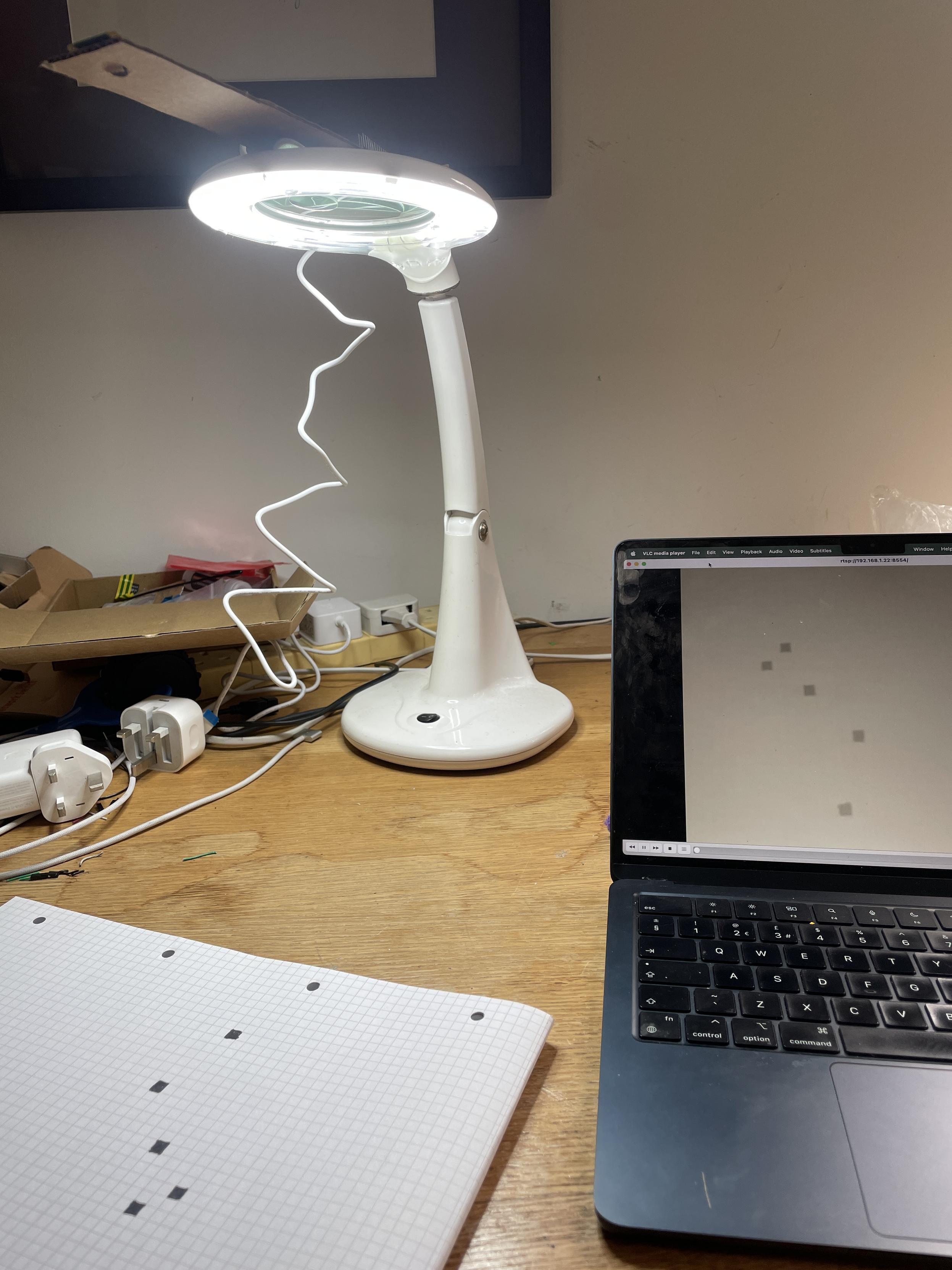 a pi zero taped to a lamp, viewing some black squares on checked paper, rtsp streamed to my laptop
