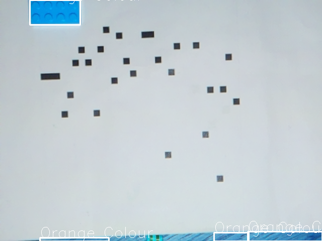 a load of black squares scattered on a white A4 sheet of paper. A blue lego piece is visible, and the text 