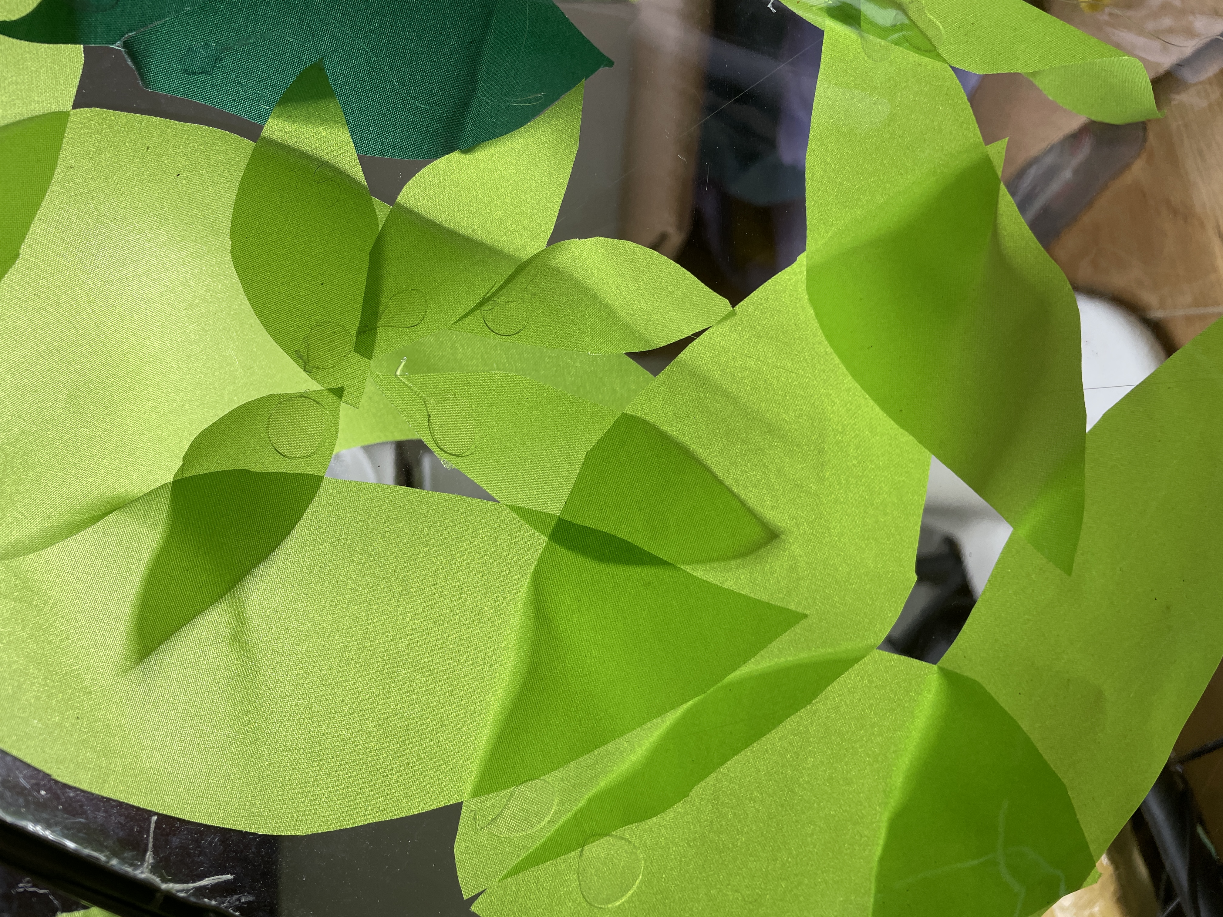vivid acid green 'leaves' cut from ripstop fabric offcuts gluegunned to a clear plastic umbrella panel. They overlap creating darker areas like real leaves.